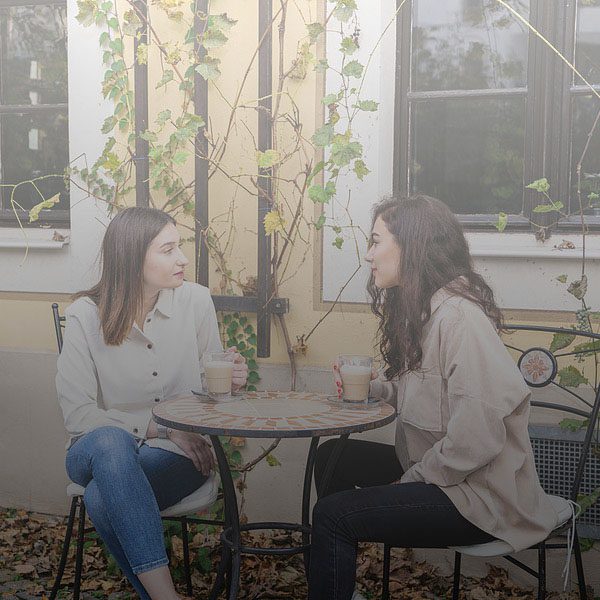 Two Young Women Talk And Drink Coffee In Cafe